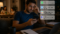 Homem sentado no sofá de casa durante a noite, olhando preocupado para o celular enquanto recebe várias mensagens de trabalho após o expediente. Ao fundo, sua família está reunida à mesa, mostrando a interferência do trabalho na vida pessoal.